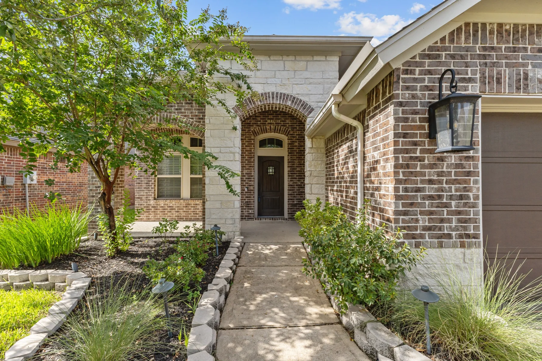 Covered front entry with brick, stone, and landscaped walkway